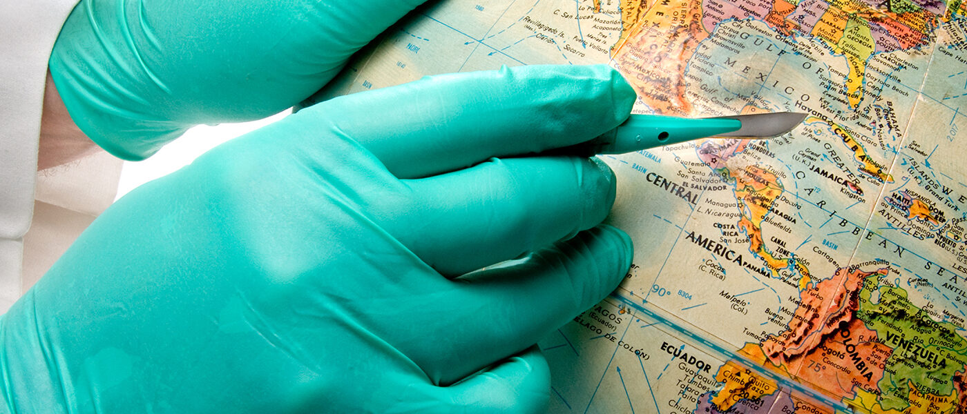 A person wearing gloves holding a scalpel pointing at a map of the world